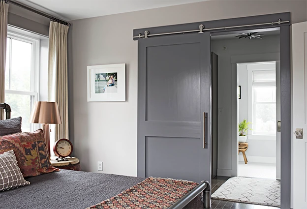 Gray painted shaker door on barn track leading to bathroom in bedroom